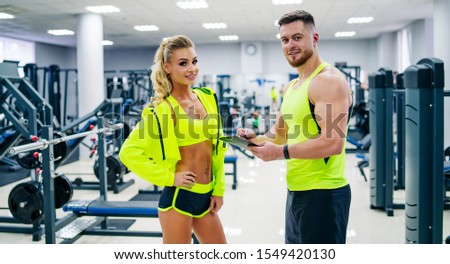 Picture of personal fitness trainer and female client in gym posing in front of the camera. Healthy life and fitness concept.