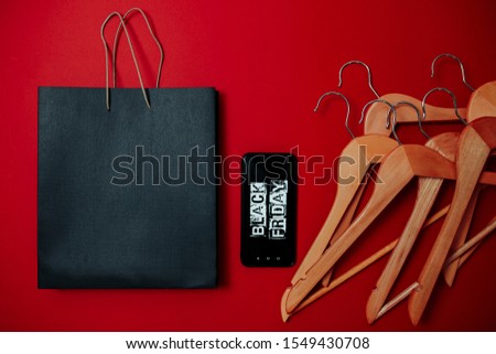 Black friday image with space for text. Bkack friday sale flat lay. Black friday bag. Hangers, black bag and mobile phone on the red background.