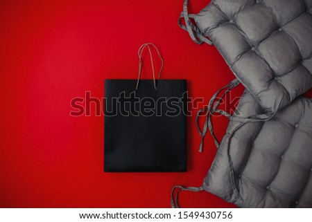 Black friday image with space for text. Bkack friday sale flat lay. Banner for home goods shop. Soft gray pillow and black bag on the red background.