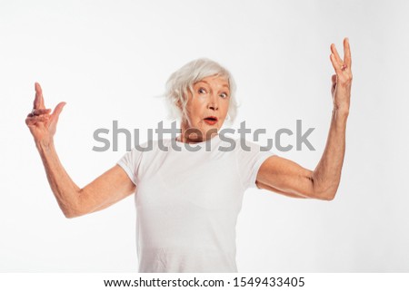 Amazing old woman perform alone on camera. Looks wondered and wave with hands. Actress. Wear white shirt. Female elder playing alone. Isolated over white background