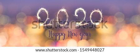 Happy new year 2020 written with sparkles on panoramic banner of blurred bokeh holiday lights at night