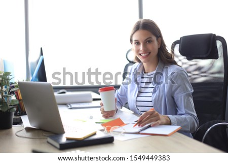 Beautiful smiling business woman is sitting in the office and looking at camera