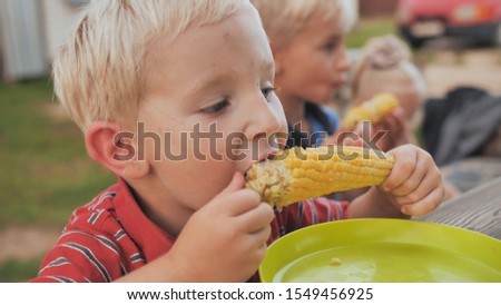 Young children eat boiled corn on village.