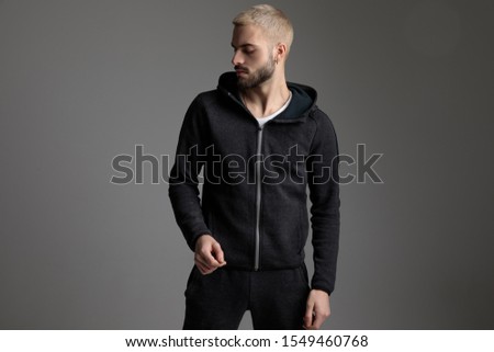 charming casual man wearing tracksuit standing and looking aside serious on gray studio background Royalty-Free Stock Photo #1549460768