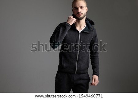 handsome casual man wearing tracksuit standing with one fist up on gray studio background Royalty-Free Stock Photo #1549460771