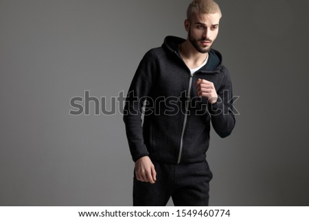 gorgeous casual man wearing tracksuit standing with loose hands and looking away serious on gray studio background Royalty-Free Stock Photo #1549460774