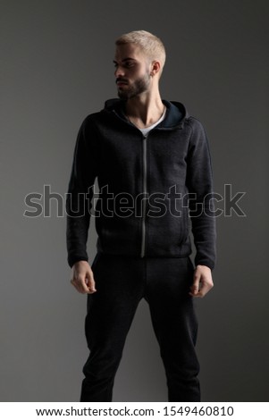 handsome casual man wearing tracksuit standing with hands loose and looking aside serious on gray studio background Royalty-Free Stock Photo #1549460810