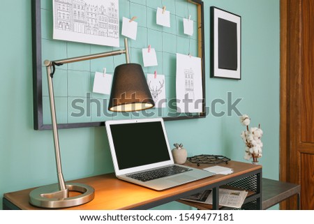 Comfortable workplace with mood board and laptop near color wall