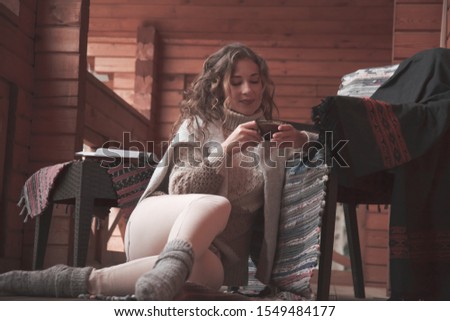 Beautiful woman relaxing with book and  cup of warm tea or coffee on armchair in wooden log house