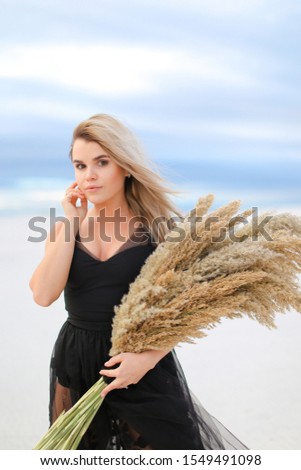 Young woman wearing black dress standing with dried plants bouquet. Concept of fashion and seasonal winter photo session.