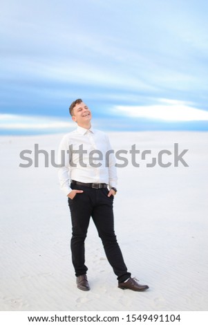 Young handsome male person standing in winter steppe and wearing white shirt, snow in backgrounf. Concept of seasonal photo session.