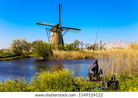 Famous windmills with fisherman in Kinderdijk village in Holland. Famous tourist attraction near Rotterdam, Netherlands.