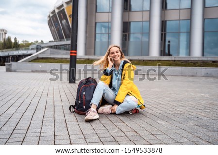 Beautiful girl calls by phone and sits on skateboard.