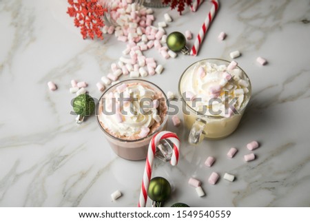 Hot dark chocolate during holiday season with whipped cream, marshmallows, candy canes, Christmas tree ornaments, green glitter balls and red snowflake on light marble background