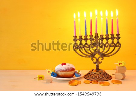religion image of jewish holiday Hanukkah with menorah (traditional candelabra), spinning top, chocolate coins and doughnut over yellow background