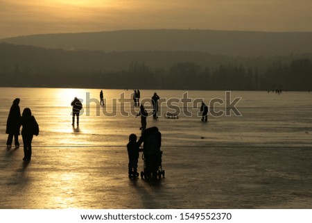 Sunset at the icy lake - The glittering sun rays painted golden shine the icy lake. Some people still skate, enjoy the sport.