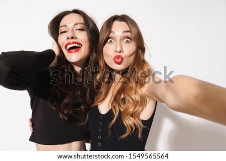 Portrait of two excited women in black clothes taking selfie photo and making kiss lips isolated over white background