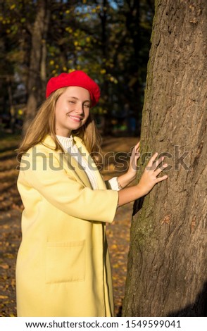 Cute teen girl in modern clothes posing in summy autumn park. Smiling blonde teenager in yellow coat and red beret  outdoors on warm day
