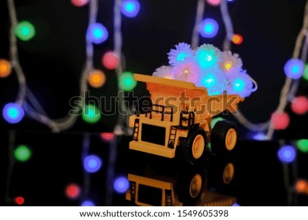 Christmas card. Happy Chrismas Concept. Children's yellow car carries bright festive garlands. Dark background, yellow color.