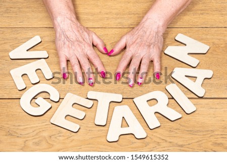 word vegetarian laid out next to female old hands lying on a wooden table