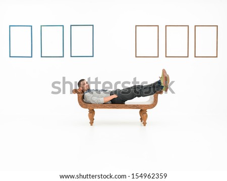 young caucasian man sitting on a wooden bench, relaxed, in front of white wall with empty frames displayed on it