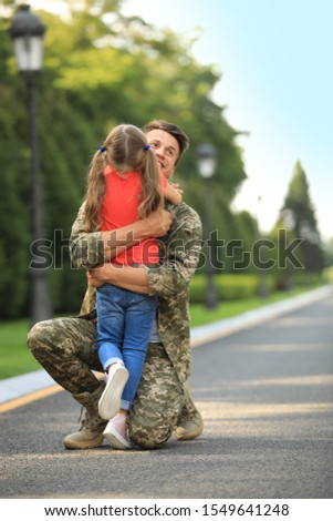 Father in military uniform hugging his little daughter at sunny park