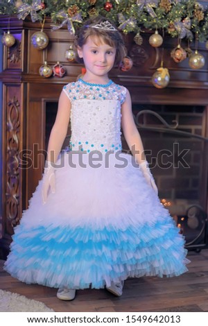 young girl with a diadem in white with a blue Christmas dress by the Christmas tree