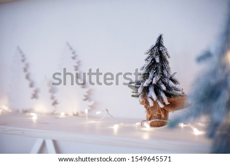 Christmas decorations. Cozy interior in pastel colors.  Figure of christmas tree coverd with snow. Multi-colored bokeh in the background