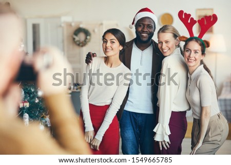 Multi-ethnic group of friends posing for photograph during Christmas party, all wearing Santa hats and costumes, copy space