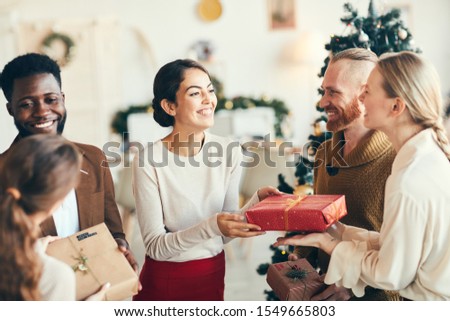 Group of elegant young people exchanging gifts and smiling cheerfully during Christmas party, copy space