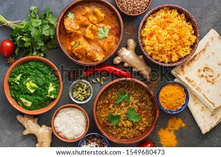 Assorted Indian food on a dark rustic background. Traditional Indian dish Chicken tikka masala, palak paneer, saffron rice, lentil soup, pita bread and spices. Top view, flat lay Royalty-Free Stock Photo #1549680473
