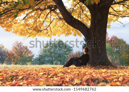 Man sitting under majestic orange cherry tree at autumn park at sunset. Dramatic colorful fall scene. Landscape photography