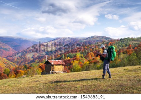 Photographer taking photo of autumn landscape with foggy peaks and orange trees. Ukrainian Carpathians mountains