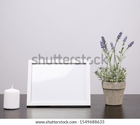 empty white frame, flowerpot with flower and candle on a black table, white background
