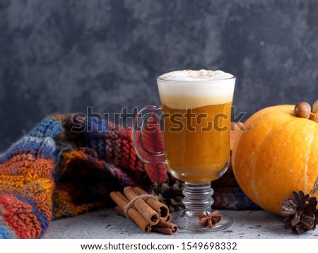 a glass of pumpkin spiced latte on the table with a colorful scarf and cinnamon and autumn leaves