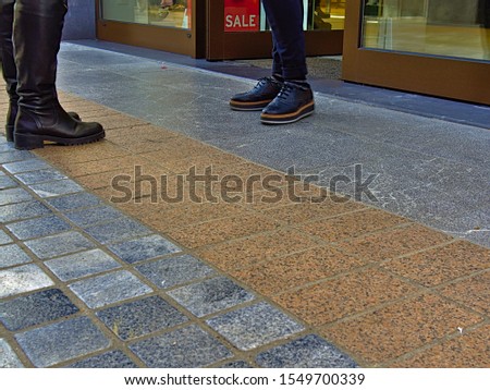 Two women legs with winter shoes outside of a shop entrance with "SALE" word on display window.