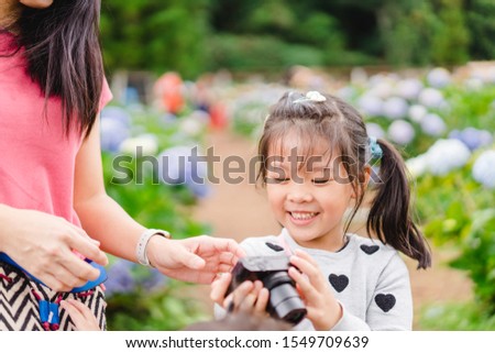5.7 years old kid girl.Little girl taking flower pictures with her mother and proudly present her picture with big smile in flower hydrangea garden in Thailand.Self esteem and Practice skill concept.