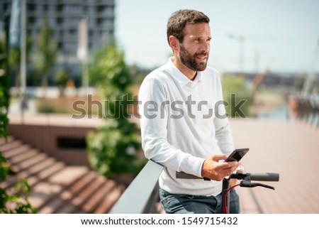 Young businessman outdoors. Handsome businessman using phone on his electric scooter