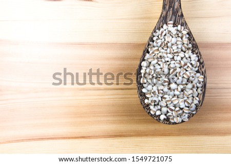 Spoon of Job's tears on wood table  background.
Adlay or millet in Wooden ladle glass bowl on tablecloth background.
Scientific name is Cox lacrima job.
top view.