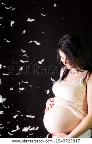 A Pregnant Young Woman Expecting a Baby and Holding gently the Tummy in a Feather Rain Background