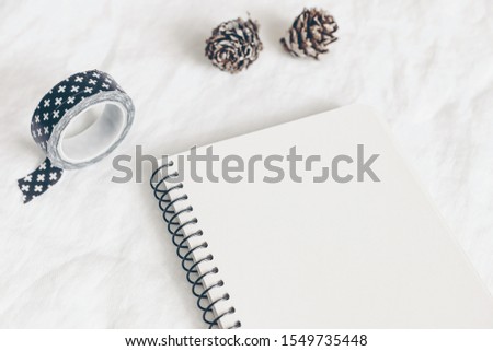 Christmas styled stock photo. Notebook, diary mockup. Still life with washi tape, larch cones on white linen background. Winter startionery. Image for blog or social media, selective focus.