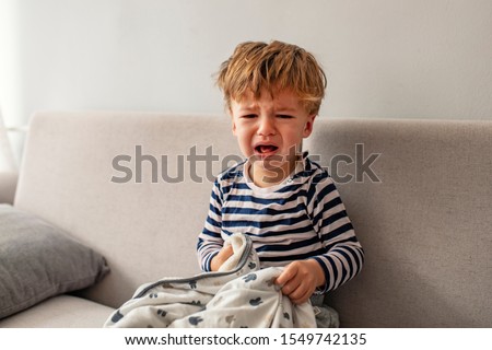 No! Little baby boy crying while seating on the couch at home. Portrait of crying baby boy. Baby's crying one year old, brunette with brown eyes, hysteria, the crisis of the first year of life Royalty-Free Stock Photo #1549742135