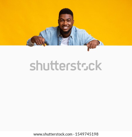 Free Space For Advertising. African american man leaning on empty white board and pointing on it, yellow background.
