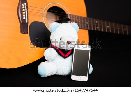 Blue teddy bear holding a phone, with a guitar in the background