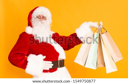 Let's go shopping, guys. Santa claus showing many paper bags with Christmas presents on orange background, panorama