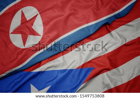 waving colorful flag of puerto rico and national flag of north korea. macro