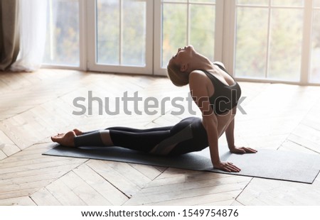 Athletic young woman making cobra pose on yoga mat, exercising in studio, copy space