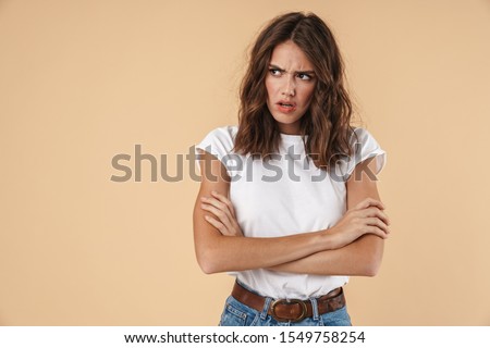 Portrait of a lovely angry young girl wearing casual clothing standing isolated over beige background, arms folded Royalty-Free Stock Photo #1549758254