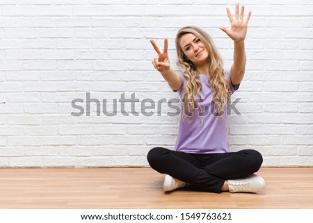 young blonde pretty woman smiling and looking friendly, showing number seven or seventh with hand forward, counting down