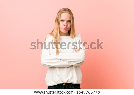 Young blonde teenager woman blows cheeks, has tired expression. Facial expression concept.